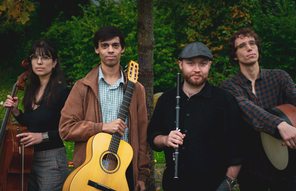 groupe de musiciens, de gauche à droite : une femme brune avec une contrebasse, un homme brun avec une guitare, un homme avec une casquette et une flûte et un homme aux cheveux châtains abec un tambour - Agrandir l'image, fenêtre modale