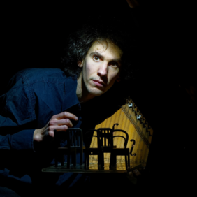 un homme avec une chemise bleue manipule une maquette miniature de piano avec des chaises