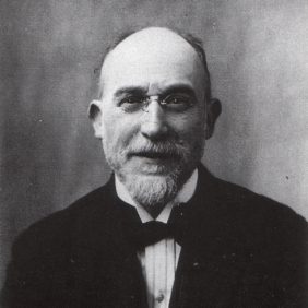 Portrait ancien, en noir et blanc, d'un homme en costume portant des lunettes, une barbe et ayant le crâne